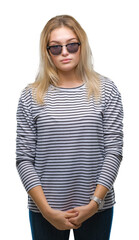 Young caucasian woman wearing sunglasses over isolated background with serious expression on face. Simple and natural looking at the camera.