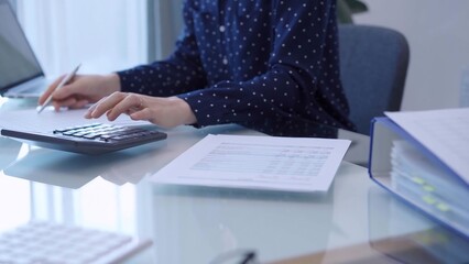 A female accountant with blue dotted blousy is using a laptop computer and calculator to calculate...