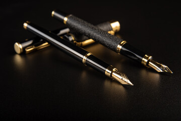 Fountain pens, beautiful black and gold fountain pens, positioned on dark background, selective...