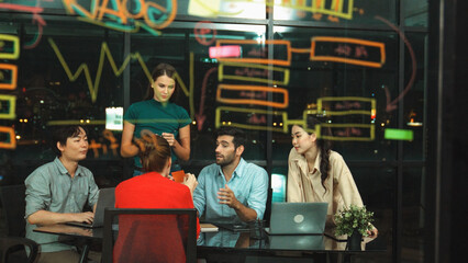 Skilled business team discussion about start up project at office. Group of businesspeople talking, explaining, sharing, brainstorming marketing idea at night office with skyscraper. Tracery