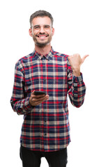 Young hipster adult man holding smartphone pointing and showing with thumb up to the side with happy face smiling