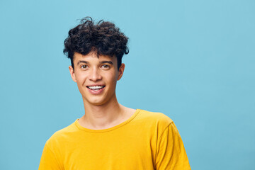 Smiling young man with curly hair wearing a yellow t shirt against a light blue background, showcasing a positive and cheerful expression, ideal for uplifting content and lifestyle themes