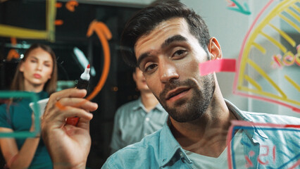 Skilled male leader explain statistic graph by drawing and writing on glass wall. Smart businessman...