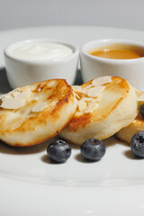 Appetizing cheese pancakes with blueberries and honey on a large white plate