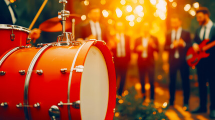 A vibrant orange drum in the foreground with a band playing in a sunlit outdoor setting, creating a festive atmosphere.
