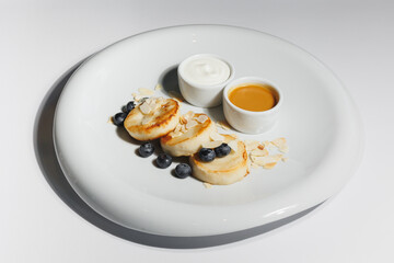 Appetizing cheese pancakes with blueberries and honey on a large white plate