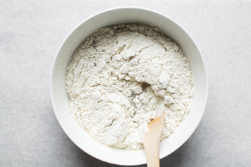 Overhead view of nigerian puff-puff dough being mixed with a wooden spoon, puff-puff dough in a white mixing bowl, process of making puff-puff or bofrot