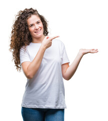 Beautiful brunette curly hair young girl wearing casual t-shirt over isolated background amazed and smiling to the camera while presenting with hand and pointing with finger.