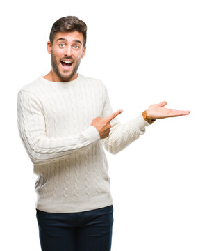 Young handsome man wearing winter sweater over isolated background amazed and smiling to the camera while presenting with hand and pointing with finger.
