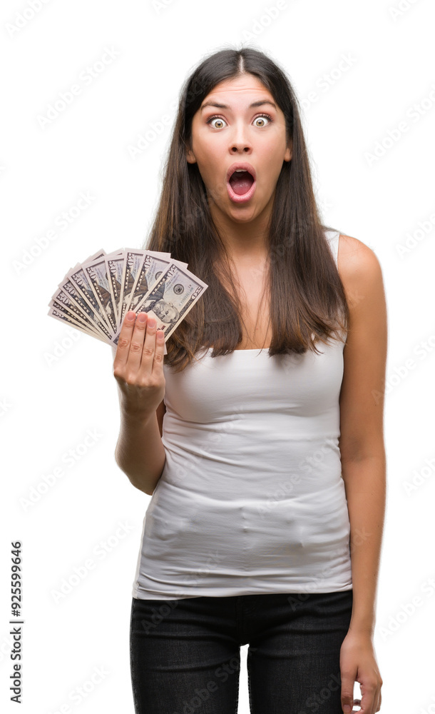 Sticker Young hispanic woman holding dollars scared in shock with a surprise face, afraid and excited with fear expression