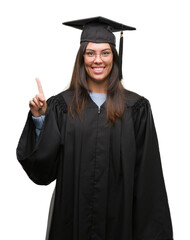 Young hispanic woman wearing graduated cap and uniform showing and pointing up with finger number one while smiling confident and happy.