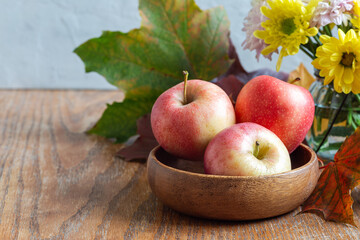 Apples in bowl, flowers and fall leaves on wooden table, horizontal, copy space