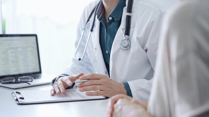 Doctor and a patient. The physician, wearing a white medical coat over a green shirt, is gesturing...