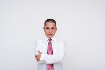 A serious manager with arms crossed. A middle aged asian man looking sternly at camera. Wearing business attire. Isolated on a white background.