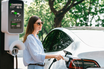 Young woman recharging battery for electric car during road trip travel EV car in natural forest or...