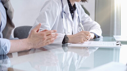 Doctor consulting patient in clinic. Female physician is writing notes while talking with a man,...
