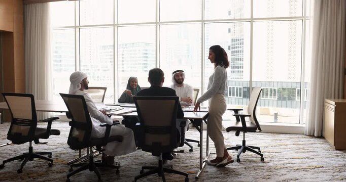 Positive young Hispanic business leader woman holding meeting with multiethnic team of Arabian and Caucasian colleagues, giving training for teamwork, effective cooperation