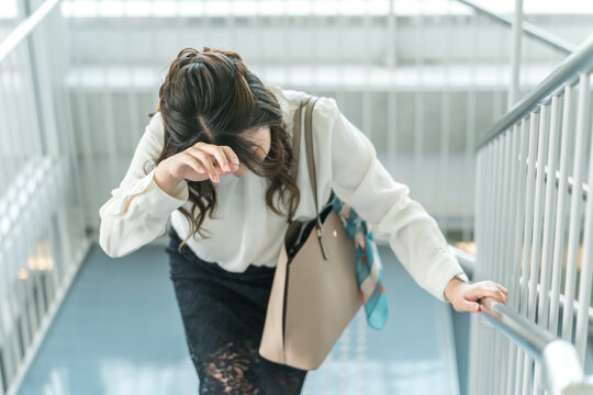 階段で体調不良になりうずくまるビジネスウーマン（貧血・立ちくらみ・目眩）
