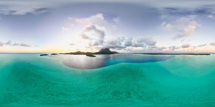 Beautiful shades of blue ocean water surrounding tropical island Bora Bora. The azure and turquoise sea is calm and inviting in French Polynesia. Panoramic drone aerial view.