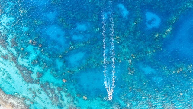 Aerial view by drone looking down on a small boat racing over azure ocean water near Bora Bora. The clear sea reveals coral reefs. 