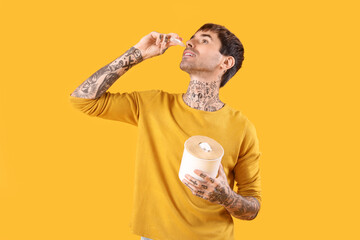 Allergic young man with tissues using nasal drops on yellow background