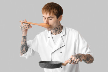 Tattooed male chef with frying pan and spoon on grey background