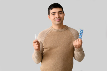 Young man with nasal drops and pills on light background