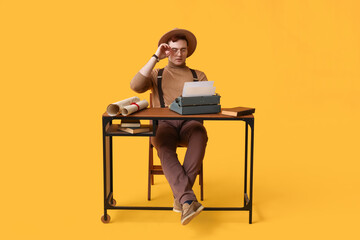 Young man with vintage typewriter at table on yellow background