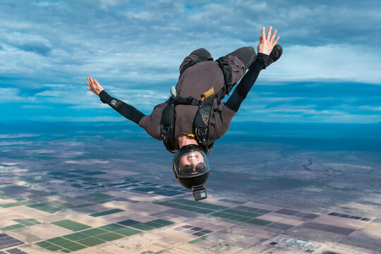 Upside down woman makes skydive alone over desert with dramatic cloudy landscape