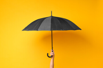 Man holding black umbrella on yellow background, closeup