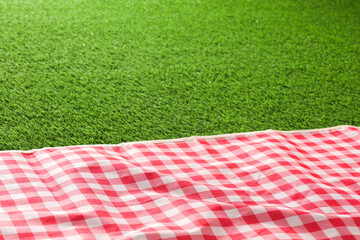 Checkered picnic tablecloth on green grass, closeup. Space for text