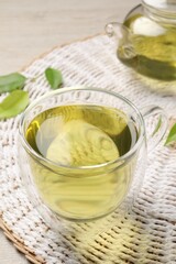Refreshing green tea in cup, teapot and leaves on table, closeup