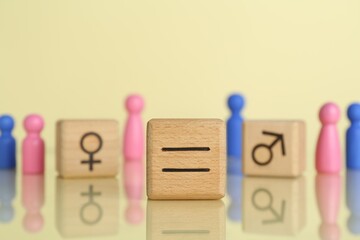 Gender equality concept. Wooden cubes with male and female figures on light yellow background,...