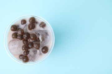 Tasty milk bubble tea in plastic cup on light blue background, top view. Space for text