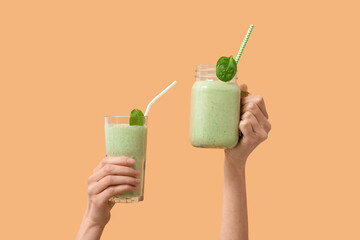 Female hands with glass and mason jar of fresh spinach smoothie on yellow background