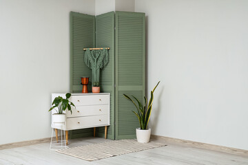 White chest of drawers with houseplants, drum and green folding screen near white wall