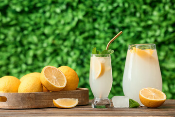 Glass and jug of fresh lemonade with mint on wooden table outdoors