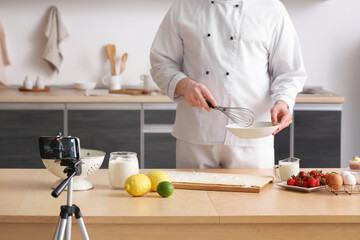 Male chef with dough and fruits recording cooking video in kitchen