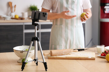 Male chef with dough and fruits recording cooking video in kitchen