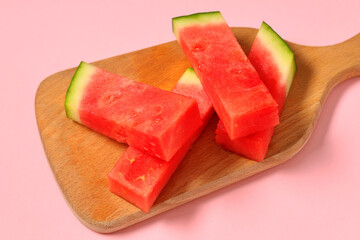 Wooden board with pieces of sweet watermelon on pink background