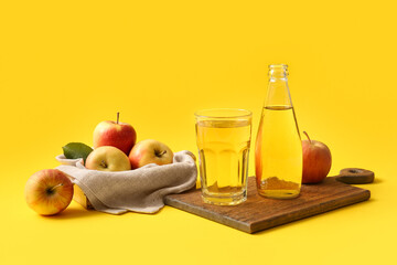 Wooden tray, bottle and glass of fresh apple cider on yellow background