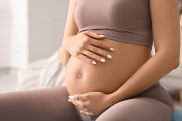 Pregnant woman in sportswear at home, closeup