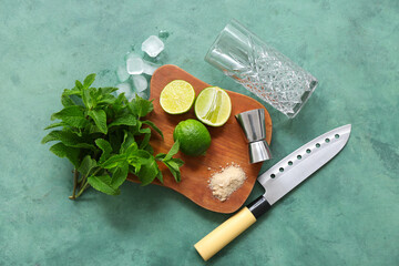 Wooden cutting board, measure cup, knife and ingredients for mojito on green background