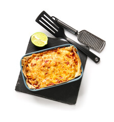 Baking dish with tasty enchilada, lime and kitchen utensils on white background