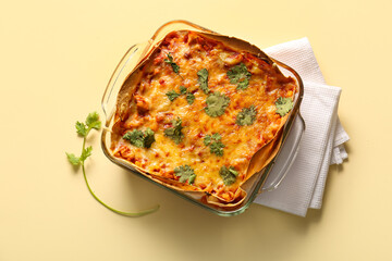 Glass baking dish with tasty enchilada and napkin on color background