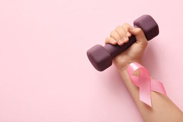 Female hand with dumbbell and pink ribbon on color background, closeup. Breast cancer awareness...