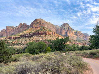 Large red rock mountains in distance with desert vegetation in foreground and footpath on the right in Zion National Park © v13llc