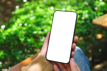 Mockup image of a woman holding mobile phone with blank white desktop screen in the outdoors