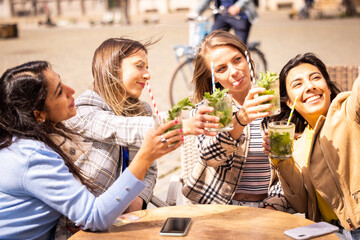 Group of four women making a toast with drinks, enjoying a sunny day outdoors, capturing the moment.