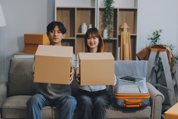 Young Asian couple relocating to a new house, joyfully packing and unpacking belongings. Expertise in moving, packing, togetherness, and creating a new home together.